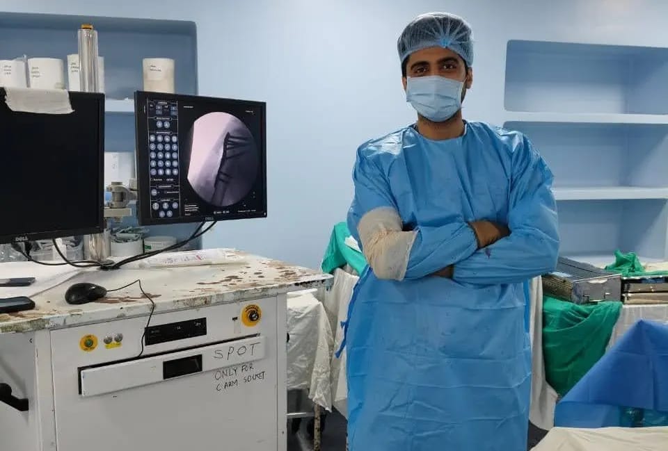 Dr. Dipen Ariwala in theatre beside an arthroscopy monitor showing the inside of a knee joint